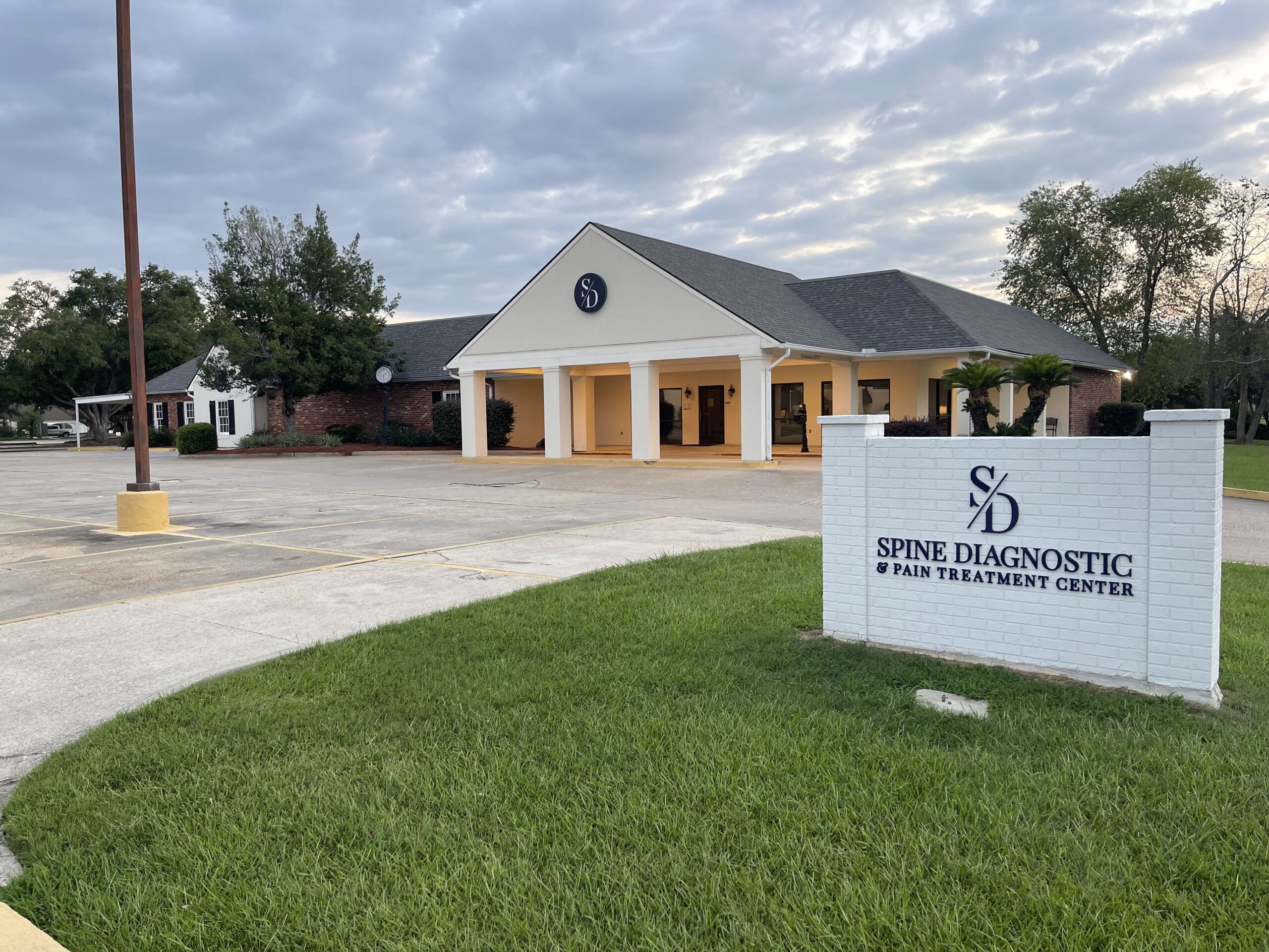 Spine Diagnostic building with white pillars and red bricks, clouds above it, and sign in front
